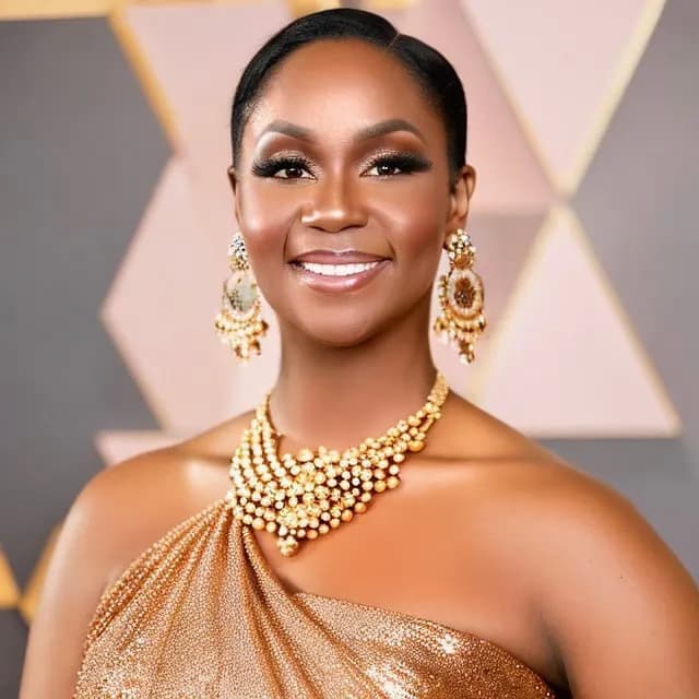 Gold drop earrings and a layered necklace against a gold one-shoulder gown, geometric backdrop.